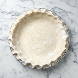 Unbaked pie crust in a glass pie dish on a marble surface