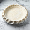 Unbaked pie crust in a metal pie dish on a white surface