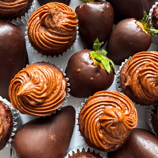 Assorted chocolate-covered strawberries and cupcakes on a white surface