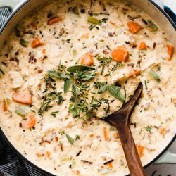 Creamy chicken and wild rice soup with carrots and herbs in a pot with a wooden spoon.